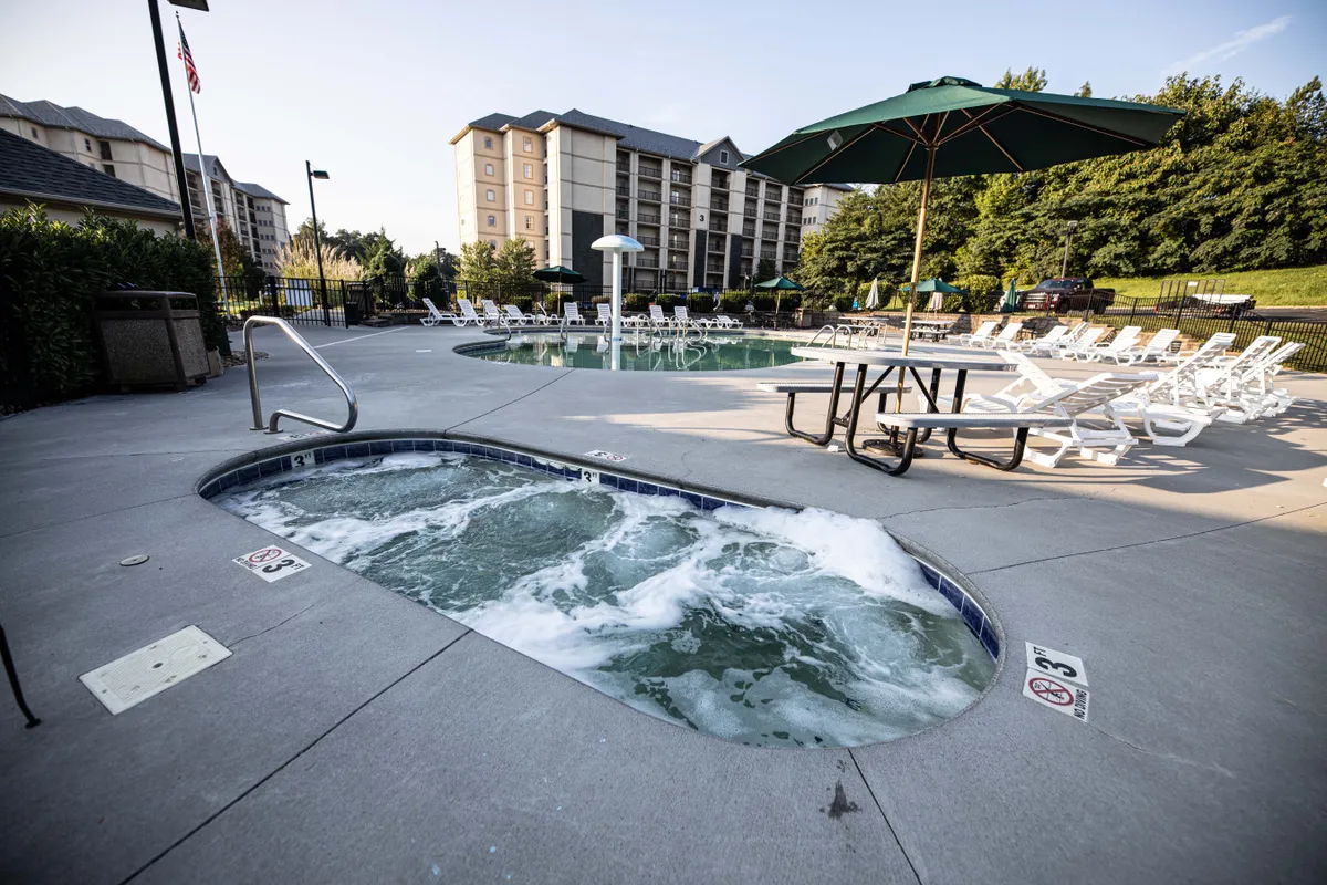 An inviting outdoor pool scene at sunset, featuring a bubbling hot tub, sparkling swimming pool, lounge chairs, umbrellas, and a picnic table where guests can socialize. The ambiance is leisurely, with families and friends enjoying relaxation and conversation by the water.