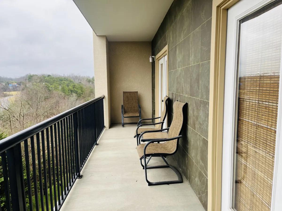 A tranquil balcony setting with comfortable chairs and a railing overlooking lush trees. The view stretches into the distance, providing a sense of privacy and a direct connection to the mountain landscape beyond.