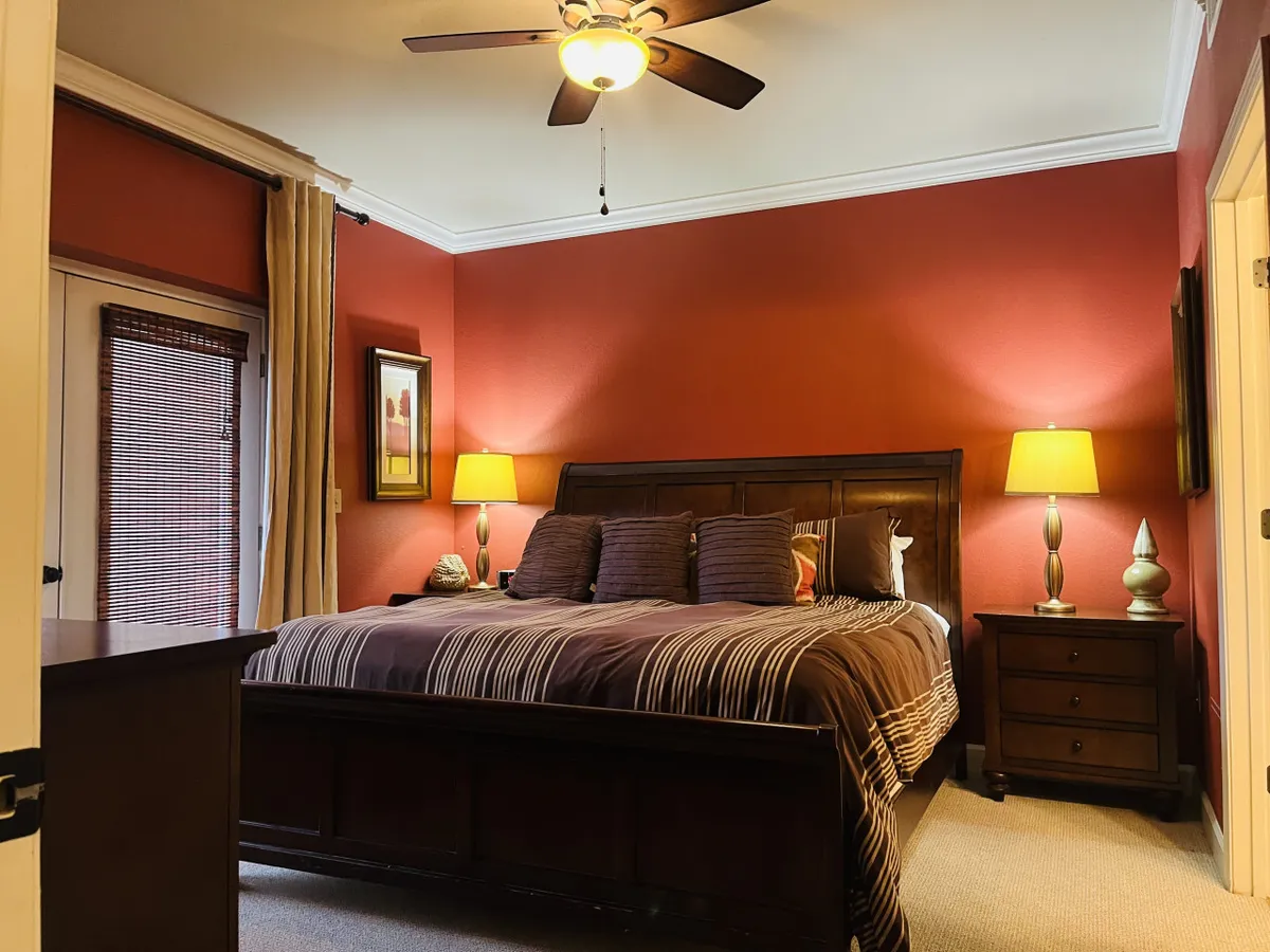 A serene bedroom featuring brown and striped bedding, two bedside lamps, framed wall art, and sturdy wooden furniture. The setting feels peaceful and comfortable, ideal for unwinding.