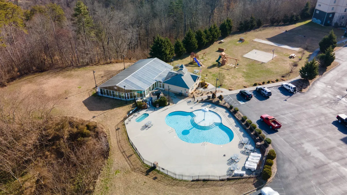 This image showcases the resort's inviting outdoor swimming pool and recreation area, with the main condo building visible in the background. The pool is surrounded by a spacious deck and green areas, suggesting ample room for families to relax and play together.