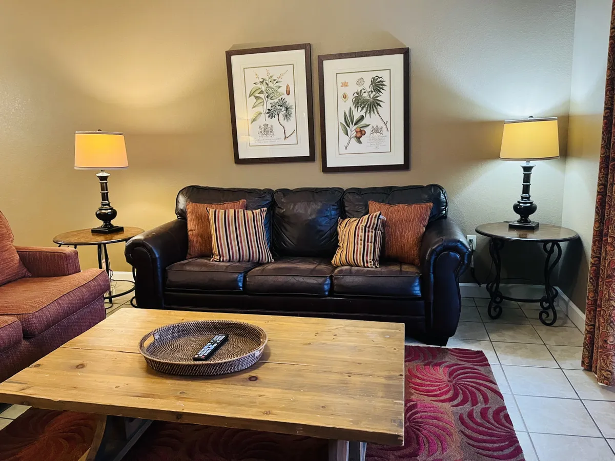 This image features a welcoming living area with a leather sofa, decorative pillows, framed botanical prints, a wood coffee table, and warm table lamps. The space looks inviting for guests to relax, socialize, or unwind after a day of exploring local attractions.