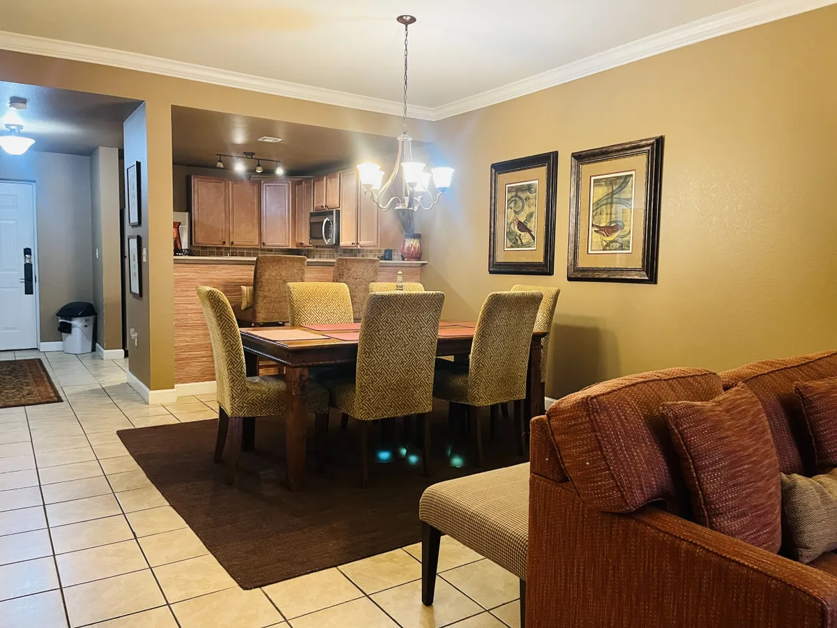 A bright, open-plan dining and kitchen area with a dining table, chandelier, sofa, and kitchen appliances. The setting suggests spaces where families can gather for meals or plan their outings.