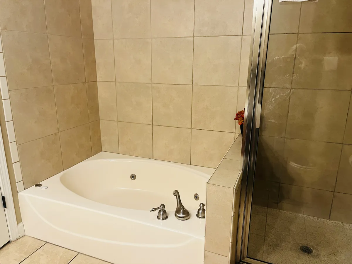A bathroom scene with a jacuzzi bathtub, glass shower enclosure, and tiled walls, exuding a sense of luxury and tranquility. The spacious layout is ideal for relaxation and self-care routines.
