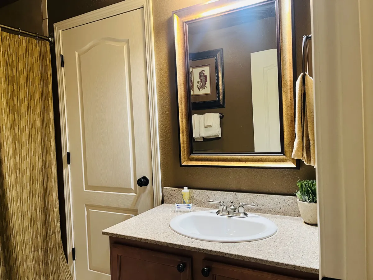 A tranquil bathroom space with a framed mirror above a sink and a neatly drawn shower curtain. The clean lines and soft lighting create a soothing, private atmosphere for daily routines.