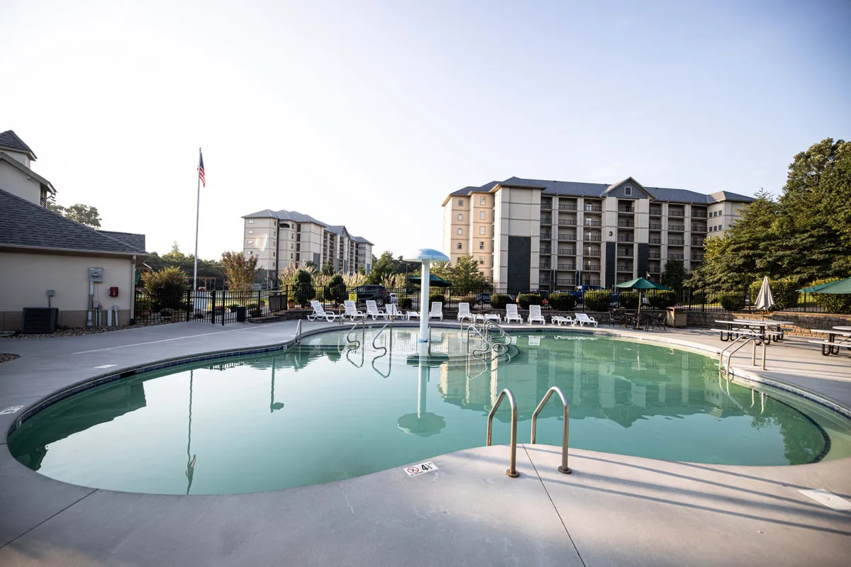 A sparkling swimming pool surrounded by lounge chairs and landscaped grounds, with the resort buildings visible in the background. The vibrant scene suggests both relaxation and social opportunities for families and groups.